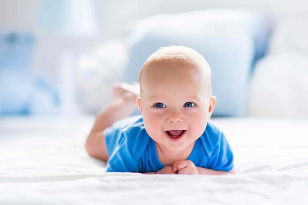 Baby in blue shirt smiling on bed
