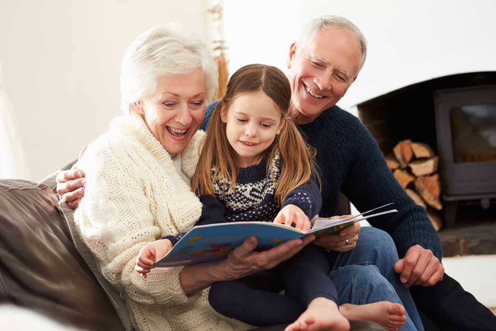 Grandparents And Granddaughter Reading Book At Home Together Relaxing